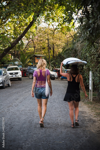 Two women walking down a road with surfboards.