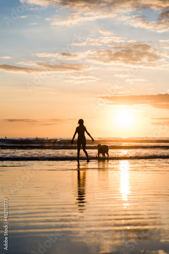 Silhouette of a woman and a dog on a beach in Costa Rica during sunset. 