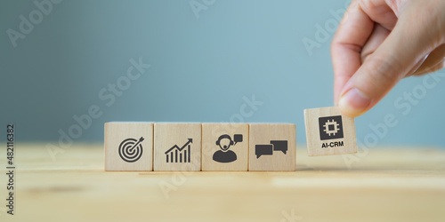 AI-CRM solution concept. Data driven marketing strategy with AI. For marketing plan, providing automated interaction to customer. Hand hold wooden cubes with AI-CRM icon on grey background, copy space photo