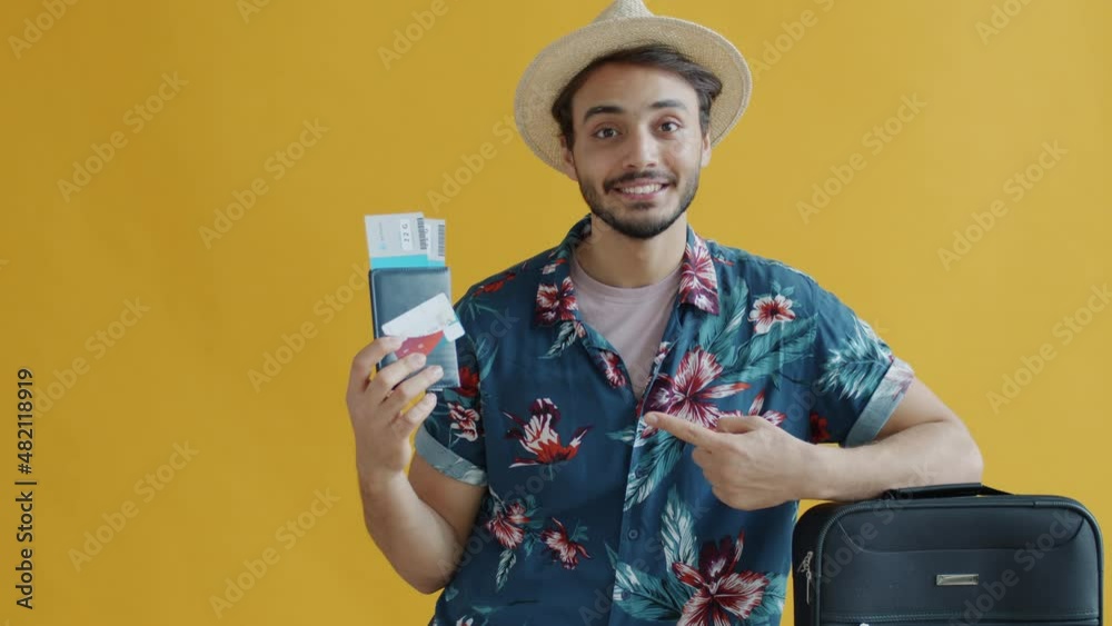 Slow motion portrait of Arab tourist holding passport travel tickets and credit card standing near luggage on yellow color background.