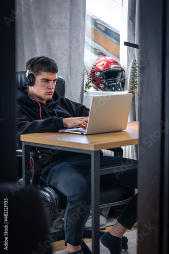 A tired teenager guy in headphones sits in front of a laptop in his room.