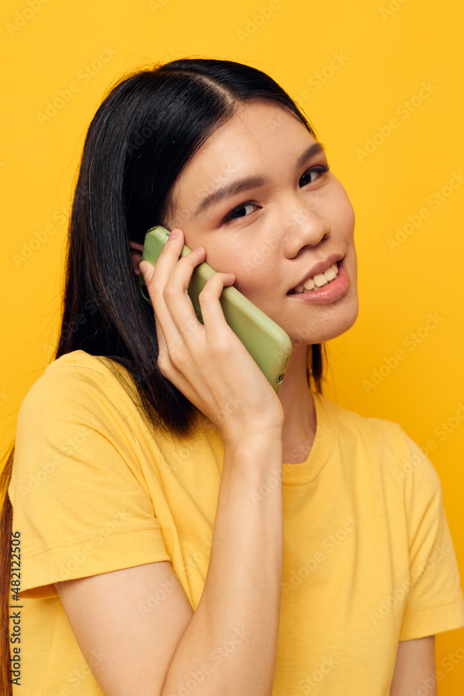 Portrait Asian beautiful young woman communicates on the phone emotions yellow background unaltered Portrait Asian beautiful young woman communicates on the phone emotions yellow background unaltered