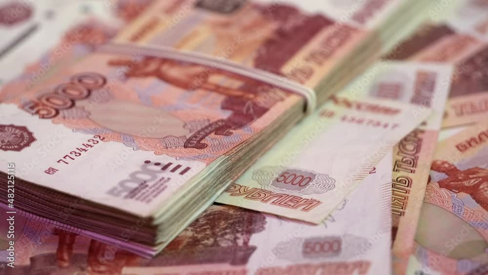 A bundle of five-thousandth Russian rubles money tied with a rubber band lies on a rotating platform covered with banknotes of 5000 rubles. Close-up of money spinning in a circle to the right A bundle of five-thousandth Russian rubles money tied with a rubber band lies on a rotating platform covered with banknotes of 5000 rubles. Close-up of money spinning in a circle to the right
