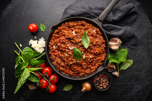 classic italian bolognese sauce stewed in a pan with ingredients on black tile background, top view