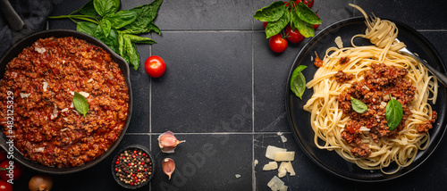 фотографія Pasta spaghetti bolognese with minced beef sauce, tomatoes, parmesan cheese and fresh basil in a plate on black tile background