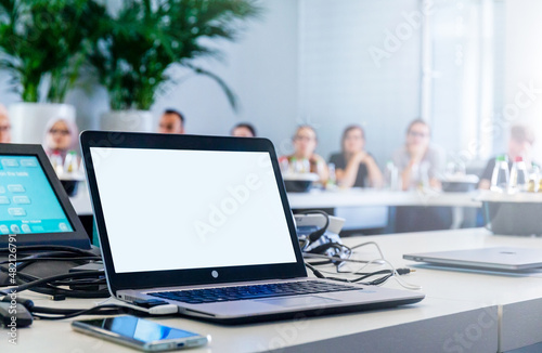 Mockup image, Laptop seht in Konferenzraum mit Teilnehmern im Hintergrund photo
