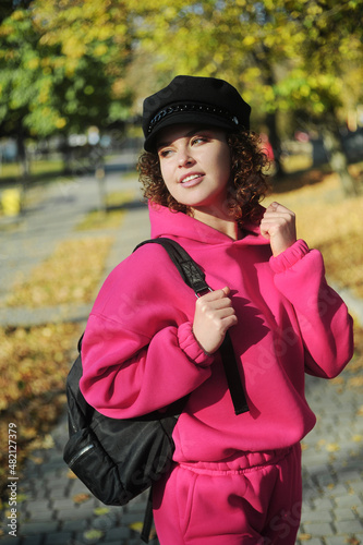 Cute curly hair woman in pink sportswear with headphones on the playground