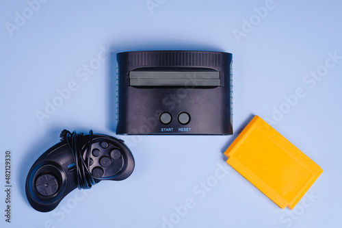 Old retro video game console with cartridge and joystick. Isolated on blue background. Copy space text. Flat lay. photo