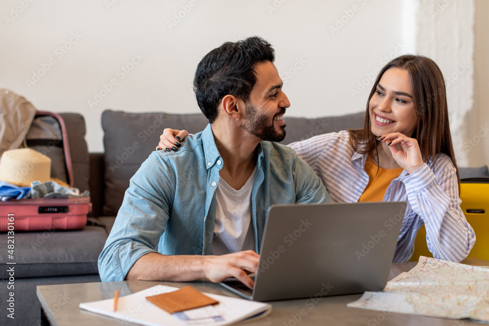Loving couple using laptop and searching best tour, packing suitcases and preparing for long-awaited vacation Loving couple using laptop and searching best tour, packing suitcases and preparing for long-awaited vacation