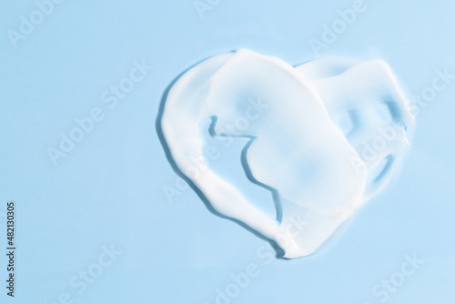 Smear of cream in the shape of a heart on a blue background with copy space. Beauty concept.