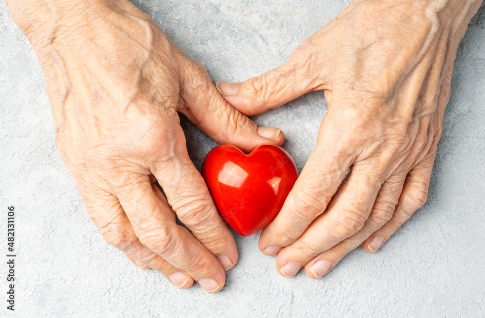 Taking care for the elderly concept with a wrinkled hands holding red heart symbol. Taking care for the elderly concept with a wrinkled hands holding red heart symbol.