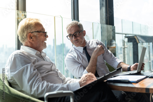 Two business partner discuss their business plan with each other. They have their favorite drink with them. They are in a hotel lobby with beautiful cityscape scene behind them.