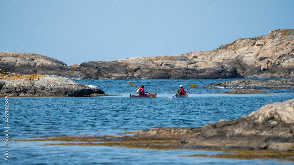 Two Adventurous kayakers paddles and explore the famous Island Marstrand. Bay of granite rocks and crystal clear Blue Ocean water around the Swedish West coast archipelago.