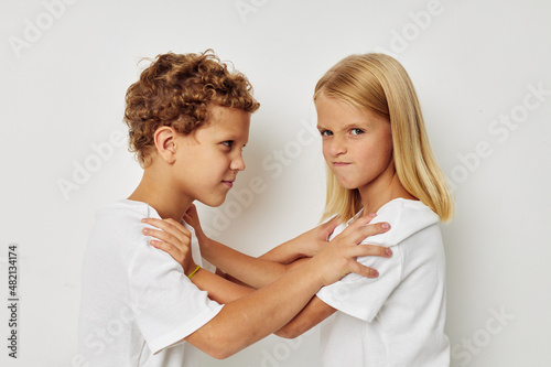 Photo of two children in white T-shirts are standing next to beige background