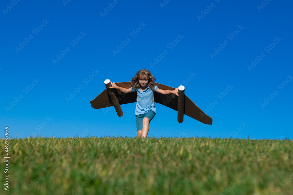 Happy child playing outside on green grass and blue sky. Kid pilot with toy jetpack. Kid boy play with toy plane cardboard. Summer travel and adventure. Success winner, imagination and dream concept. Happy child playing outside on green grass and blue sky. Kid pilot with toy jetpack. Kid boy play with toy plane cardboard. Summer travel and adventure. Success winner, imagination and dream concept.