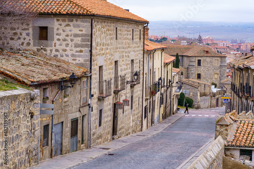 Old stone houses on a paved street overlooking the city of Avila, Spain.