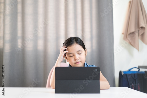 asian child headache on studying online class or kid girl student close eye to think or stressed learning on computer tablet by video call or person learn from home and hand raising or holding to head