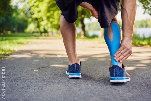 Runner holding injured achilles tendon with kinesiology tape photo