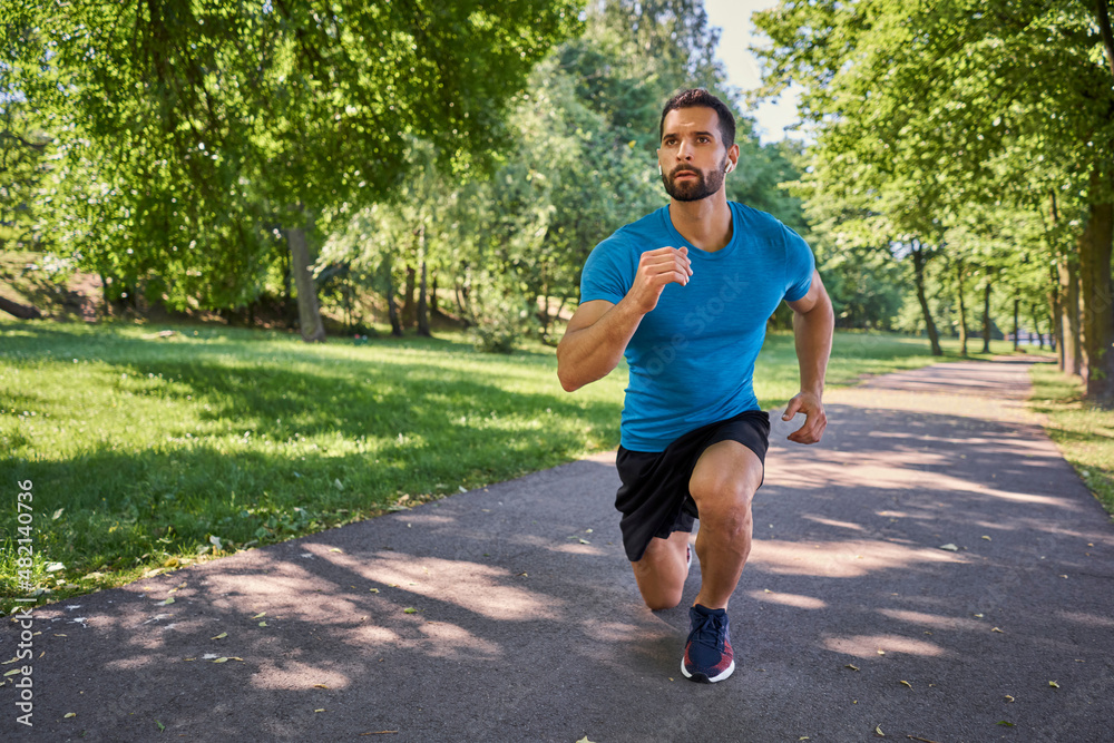 Young man exercises lunges during a workout outside in a park Young man exercises lunges during a workout outside in a park