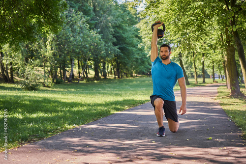 Fotografija Young man exercises kettlebell lunges during a workout outside in a park during