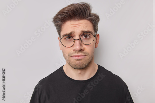 Valokuva Upset young man with bristle feels disappointed and envy regrets missing chance stands unhappy frowns face dressed casually isolated over white background
