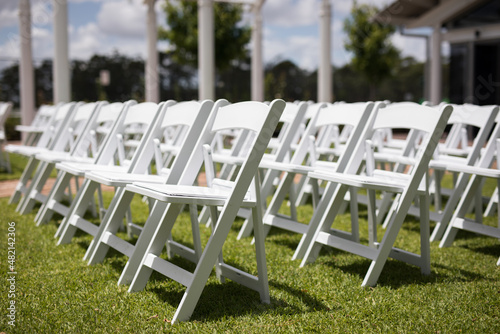 Rows white timber wedding chairs outdoors grass bright sunny day celebratrion happy gathering together love happy