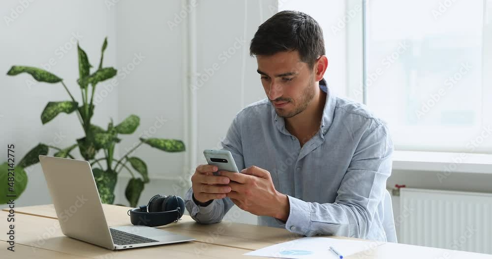 Young businessman sit at workplace desk with laptop holds cell phone ...