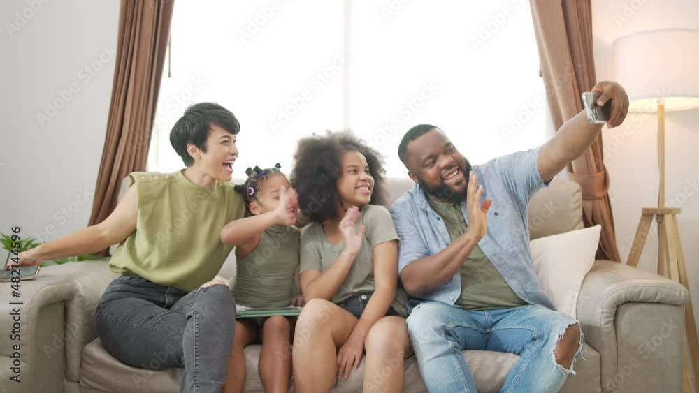 Happy African parents and two little daughter sitting on sofa in living room using mobile phone taking selfie together. Happy family enjoy and having fun leisure activity with technology at home Happy African parents and two little daughter sitting on sofa in living room using mobile phone taking selfie together. Happy family enjoy and having fun leisure activity with technology at home