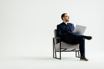 Young smiling businessman sitting in office chair and working on laptop on white background