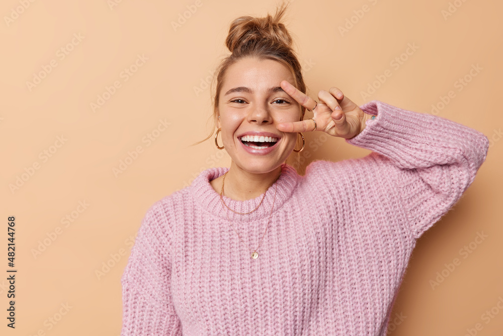 positive-young-european-woman-makes-peace-sign-over-eye-laughs-joyfully