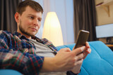 Happy man using mobile phone on a couch at home. Closeup of young man using smartphone to checking email at home, using app or social media