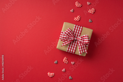 Top view photo of valentine's day decorations craft paper giftbox with checkered ribbon bow and hearts on isolated red background with empty space © ActionGP