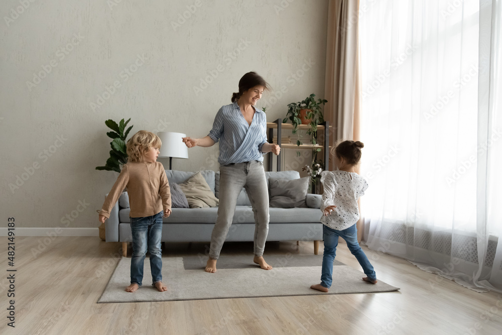 Laughing happy young single mother dancing barefoot on floor carpet with joyful little kids son daughter, listening energetic disco pop music together at home, family hobby leisure activity concept. Laughing happy young single mother dancing barefoot on floor carpet with joyful little kids son daughter, listening energetic disco pop music together at home, family hobby leisure activity concept.