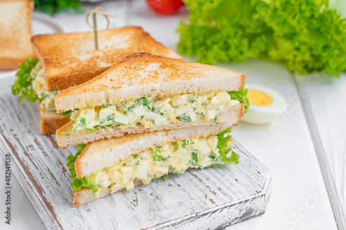 Egg salad sandwich with toasted bread and lettuce on a white wooden background. Selective focus