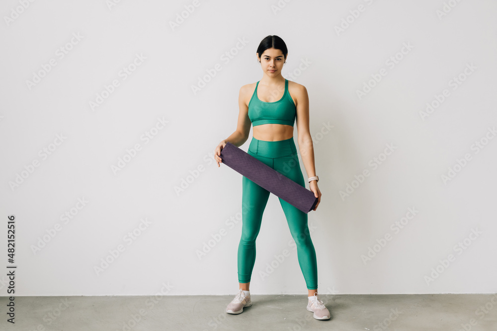 Sporty woman holding yoga mat before or after fitness class on white background