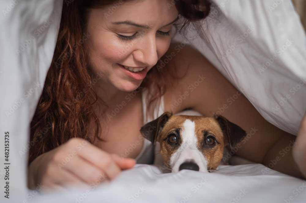 Caucasian red-haired woman sleeps in an embrace with a jack russell terrier dog on a white sheet. Caucasian red-haired woman sleeps in an embrace with a jack russell terrier dog on a white sheet.