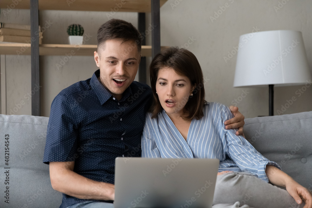 Surprised young bonding family couple looking at computer screen, getting email with amazing unbelievable news, reading message with online lottery gambling auction win notification, internet success. Surprised young bonding family couple looking at computer screen, getting email with amazing unbelievable news, reading message with online lottery gambling auction win notification, internet success.