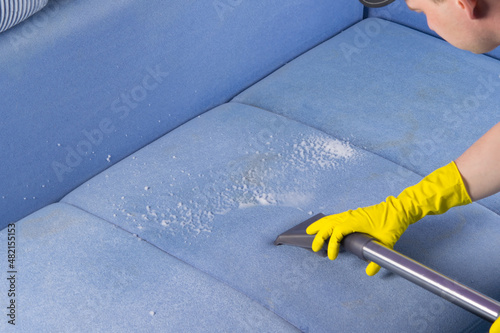 specialist in protective gloves, cleans the soiled surface of the sofa with a washing vacuum cleaner and foam photo