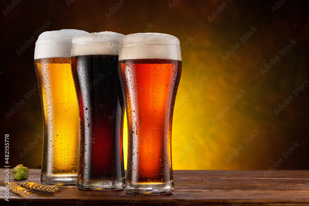 Cooled glasses of  three different beer on the wooden table. Dark brown background.