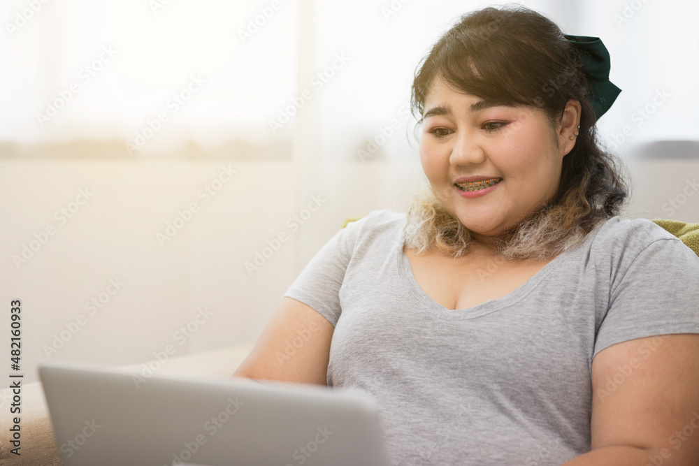 Body positive plus size female using laptop to video conference and working quarantine stay at home. Happy women's plus size video call in living room. Body positive plus size female using laptop to video conference and working quarantine stay at home. Happy women's plus size video call in living room.
