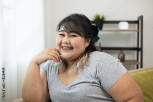 Happy women's plus sitting on sofa in living room. Body positive plus size female lives happily and is proud of herself.