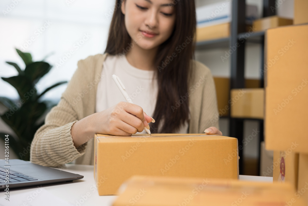 Young asian business woman writing address to sending product to customer. Online business working at home. Startup Small business owner entrepreneur Young asian business woman writing address to sending product to customer. Online business working at home. Startup Small business owner entrepreneur