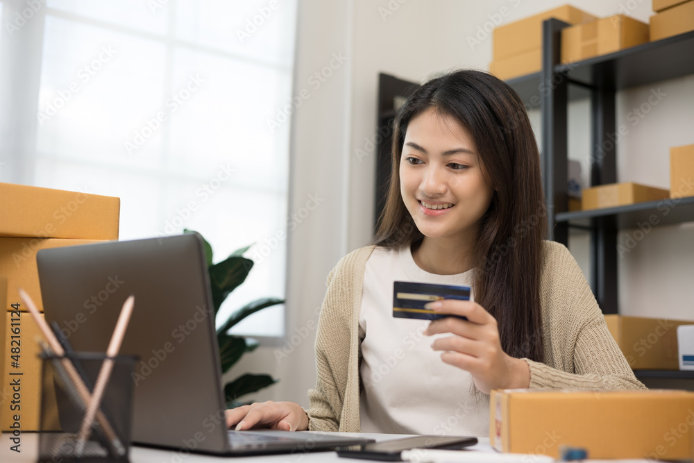Shopping online. Young asian woman input the serial number of credit card to laptop for shopping payment. Buy item online delivery at home. Small business entrepreneur with many parcel box on table Shopping online. Young asian woman input the serial number of credit card to laptop for shopping payment. Buy item online delivery at home. Small business entrepreneur with many parcel box on table