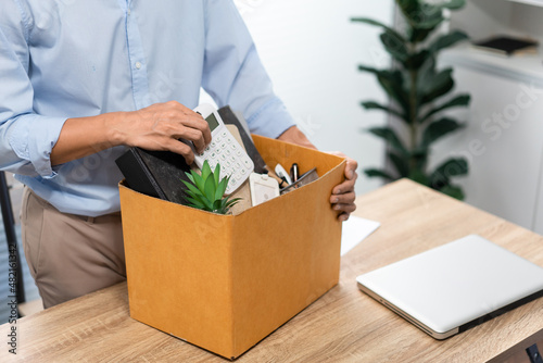 Resignation Concept The man in light blue shirt standing at the desk and putting the calculator and other stuff into the box © snowing12