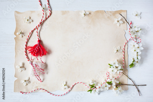 Flowering branches of cherry plum, red-white martenitsa with tassels and paper for text for the holiday of March 1, white wooden background. photo