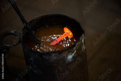 blacksmith with working tools puts a hot melal nail in the water photo