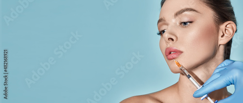 Lips filler injection for beautiful woman's lip augmentation with beautician on blue background. Lip augmentation procedure