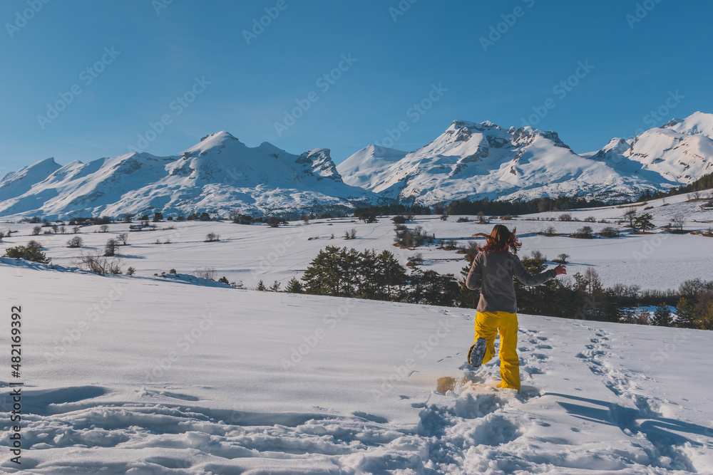A full-body back view shot of an unrecognizable young Caucasian woman running towards the French Alps mountains (La Joue du Loup, Devoluy)