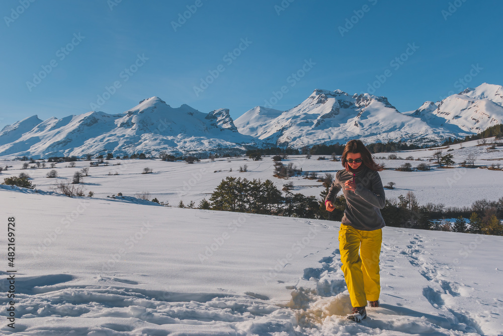 A full-body shot of a young Caucasian woman running towards the camera in the French Alps mountains (La Joue du Loup, Devoluy)