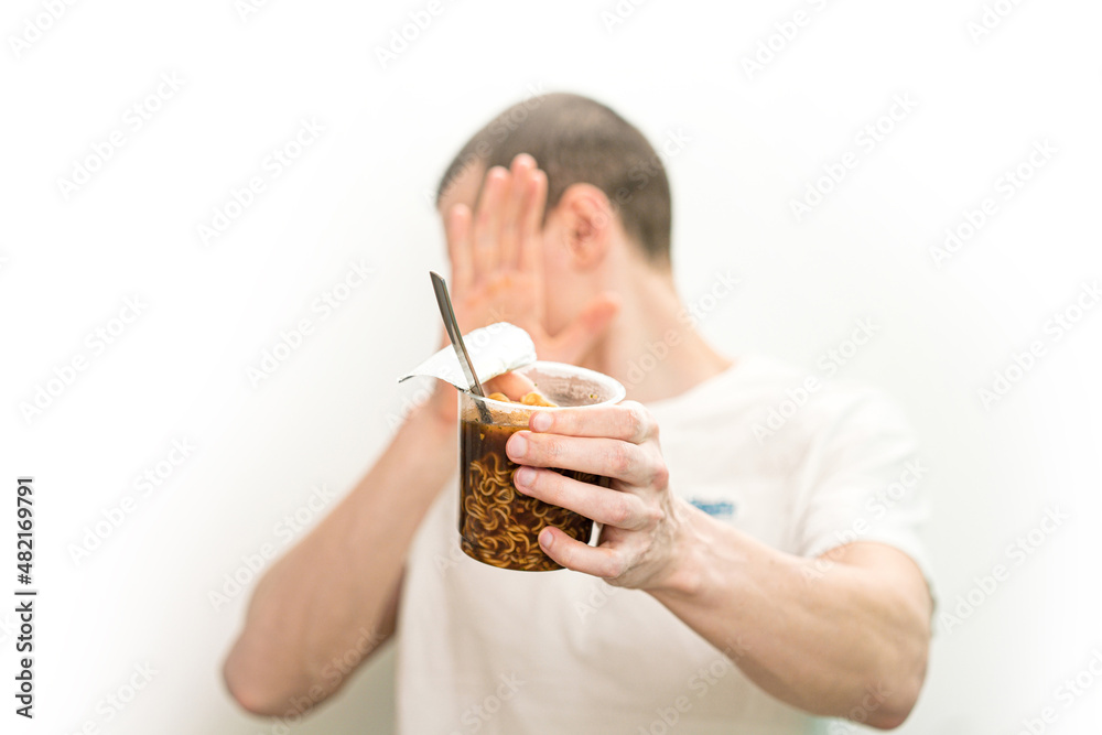Man turning away and don't want to look on fast food noodles transparent plastic cup on a white background. Refusal Harmful. Hand stop gesture. Expression. Meal Man turning away and don't want to look on fast food noodles transparent plastic cup on a white background. Refusal Harmful. Hand stop gesture. Expression. Meal
